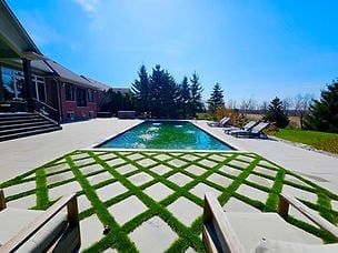 Modern backyard with geometric green and white patio leading to an elongated swimming pool under blue sky