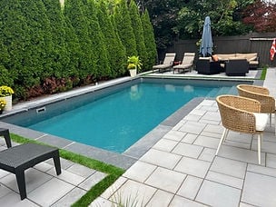 Backyard swimming pool with lounge chairs, woven seating, and patio surrounded by green hedges and landscaping